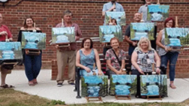 Students holding their finished Bob Ross style paintings at a Paint with Mark class in Kent