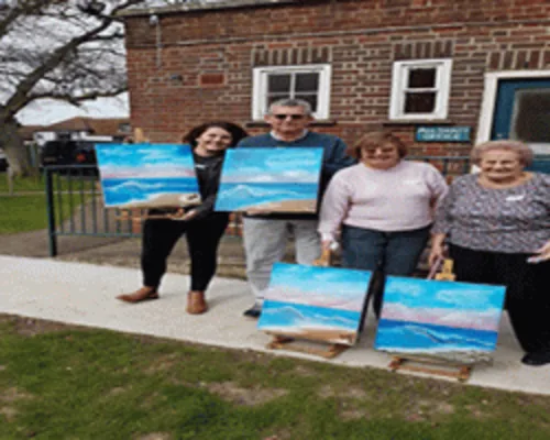 Group of painting students proudly displaying Bob Ross style mountain landscape oil paintings
