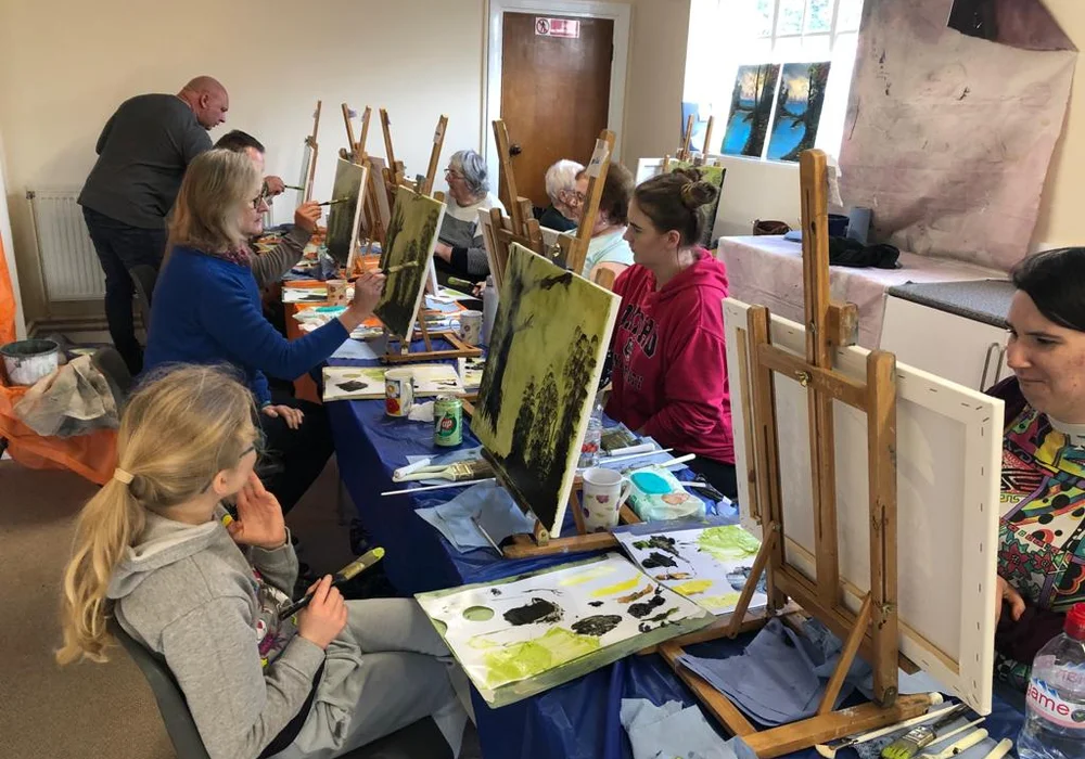 Family and young students painting Bob Ross landscapes together at an oil painting class in Kent