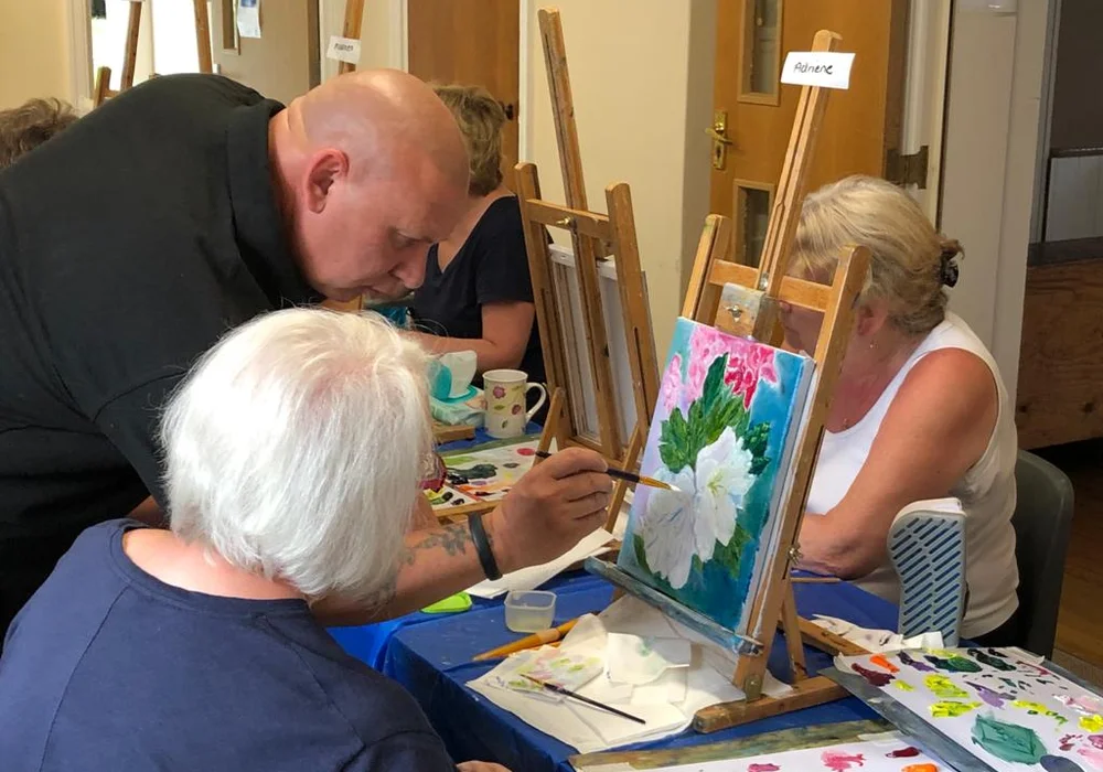 Mark Terrell helping a student paint flowers at a friendly oil painting class in Kent