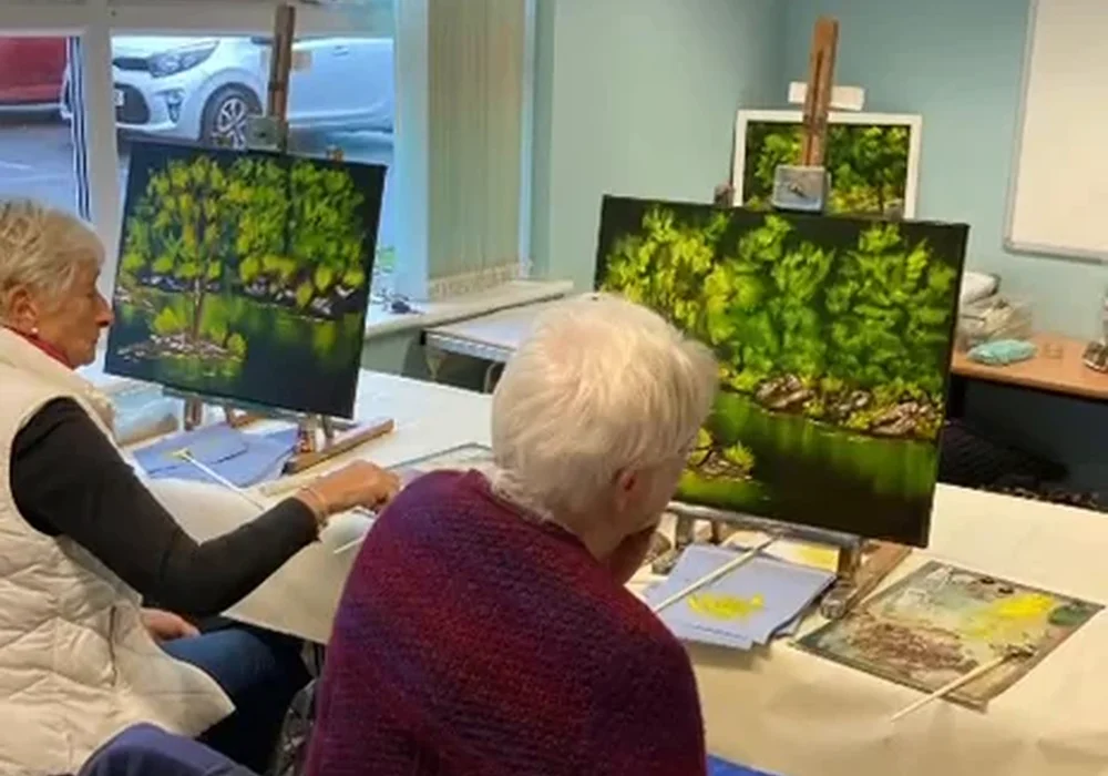 Older student painting a Bob Ross forest landscape at a friendly beginners oil painting class in Kent