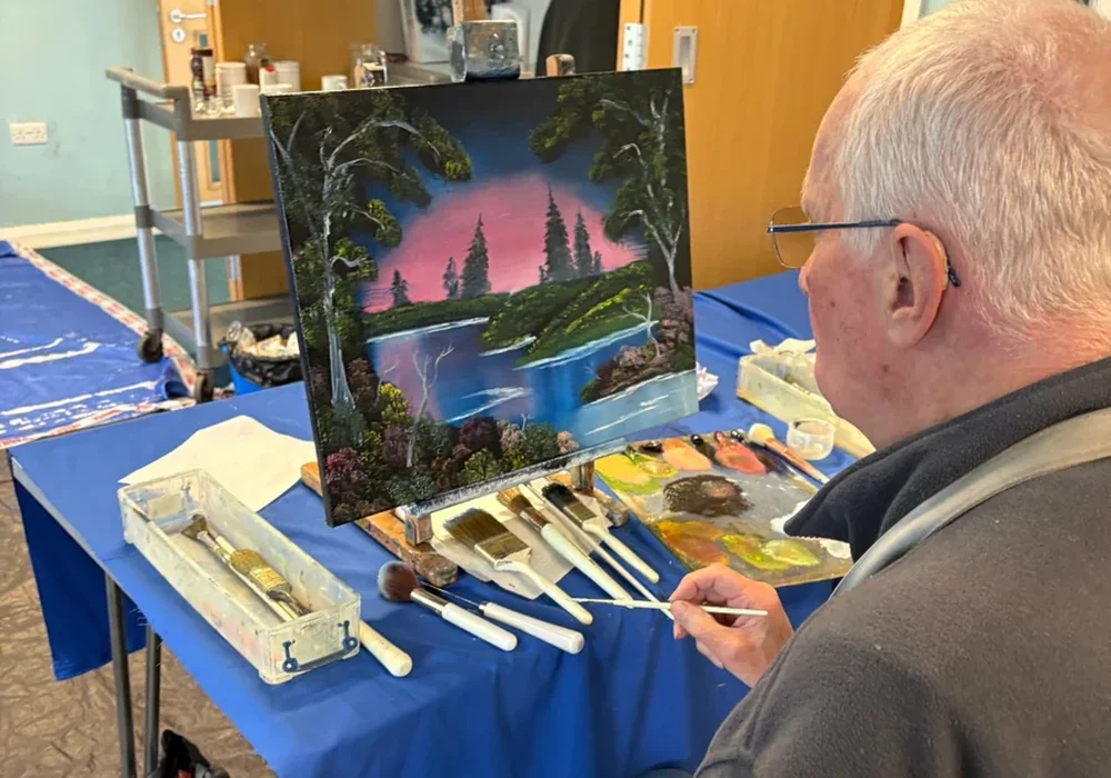 Student painting a pink sky forest lake landscape at a Bob Ross oil painting class in Kent