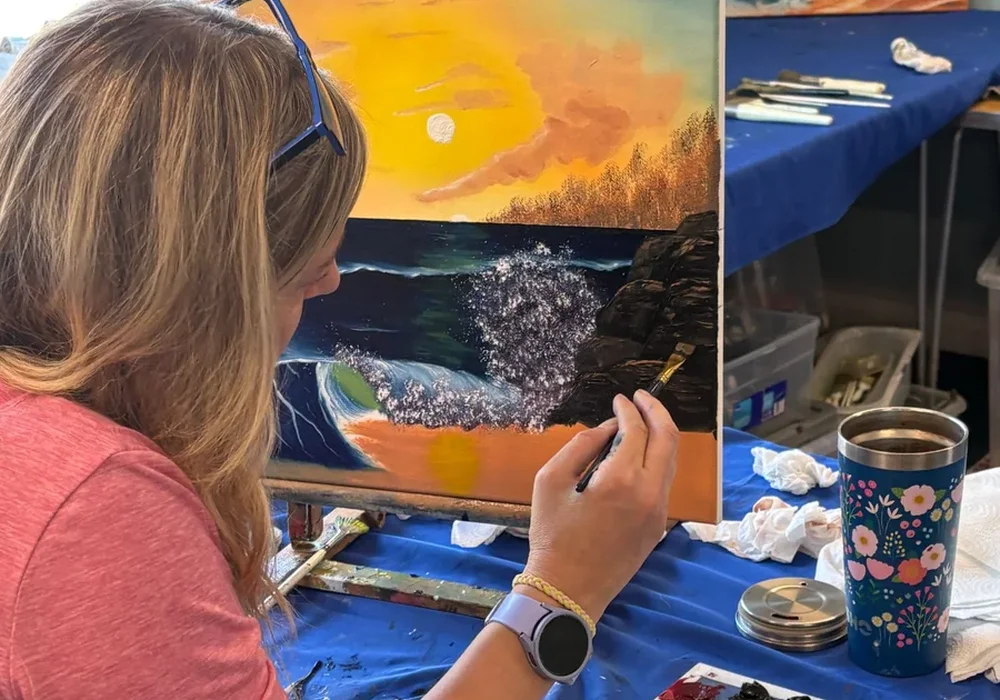 Student painting a crashing wave sunset seascape in oils at a Bob Ross painting class in Kent