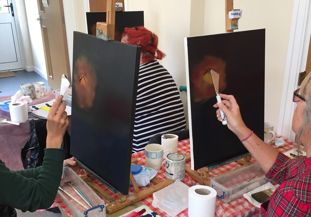 Students painting dark background canvases with a palette knife at a Bob Ross oil painting class