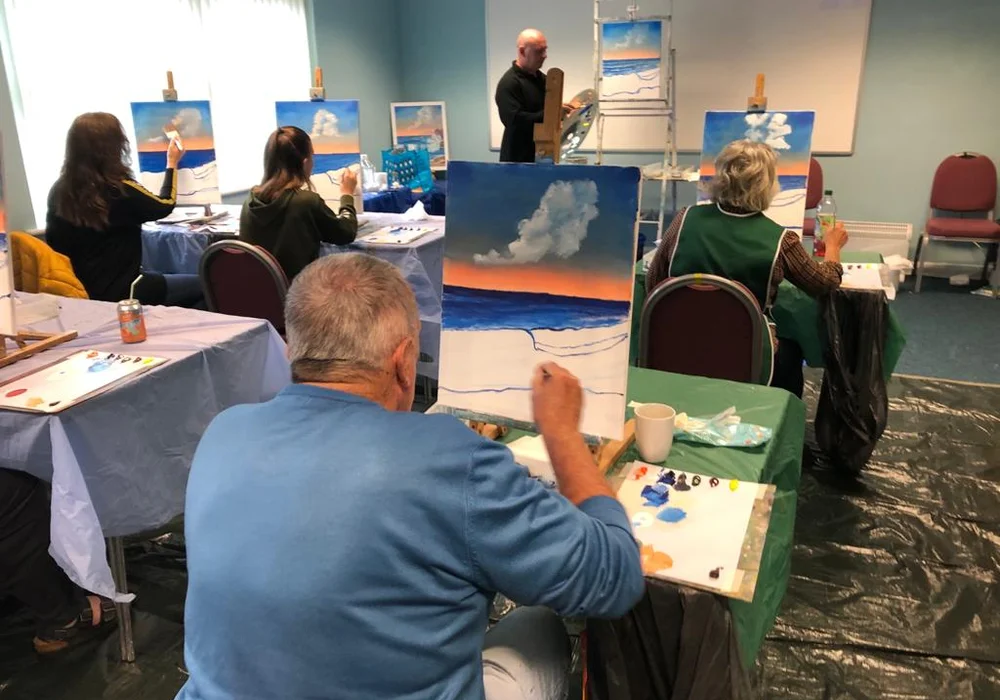 Students painting a Bob Ross sky and clouds at a wet-on-wet oil painting workshop in Kent