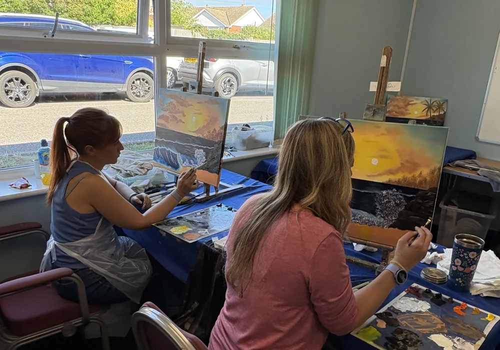 Two students painting Bob Ross sunset seascapes at a beginner oil painting class in Whitstable, Kent